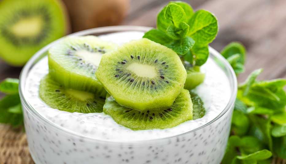 cận cảnh một bát bánh pudding chia giàu chất xơ với những lát kiwi và một nhánh bạc hà trên bàn bếp với nền là kiwi giàu chất xơ